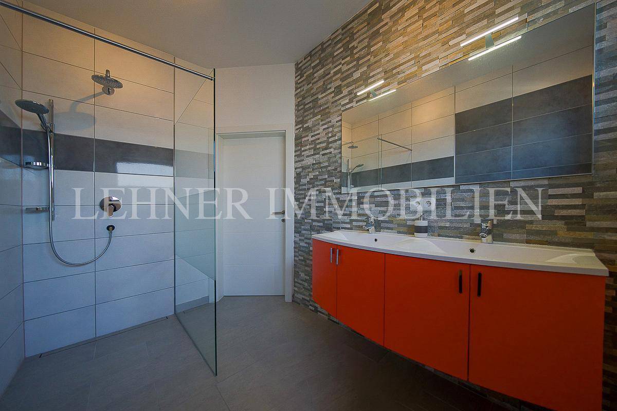 Modernes Badezimmer mit großer Duschkabine, Doppelwaschbecken und Steinwand.