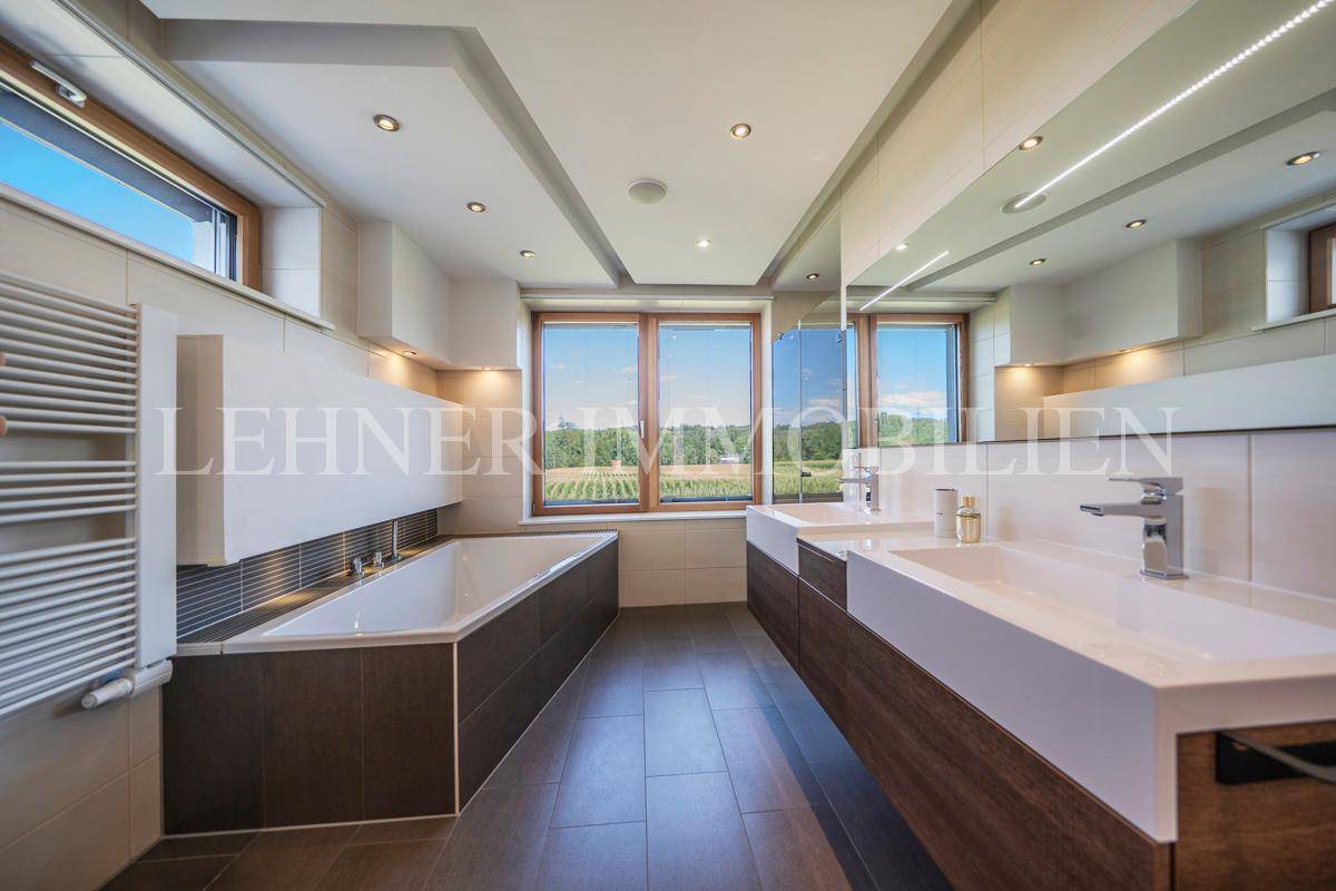 Großes, modernes Badezimmer mit Badewanne, Doppelwaschbecken und weitem Ausblick durch die Fenster.