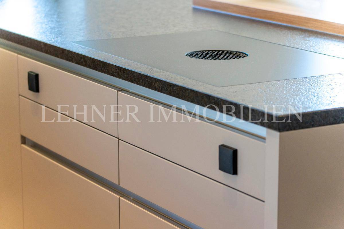 Detail der Kücheninsel mit integriertem Kochfeld und dunkler Arbeitsplatte.