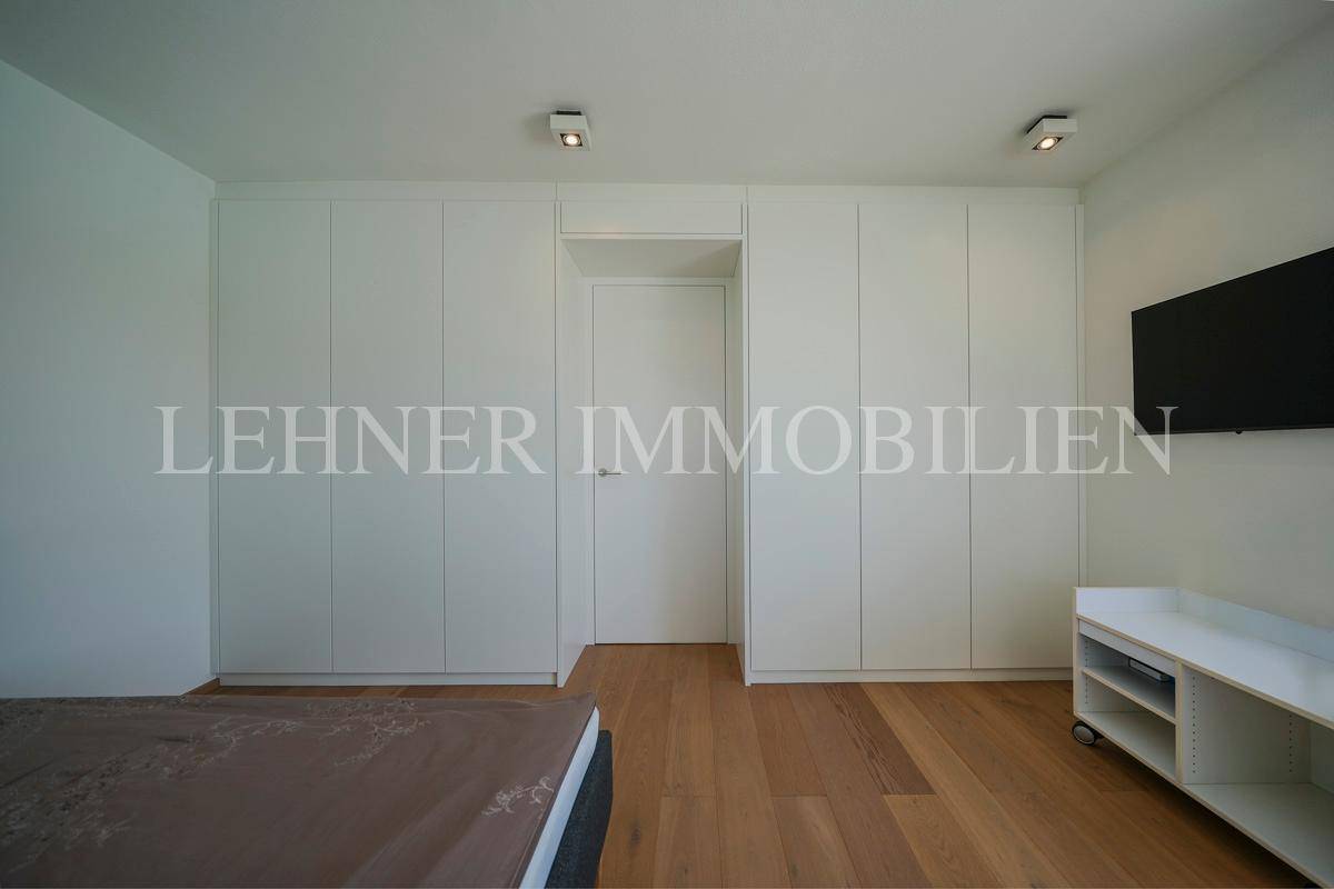 Schlafzimmer mit integrierten weißen Kleiderschränken und einem Wandfernseher.