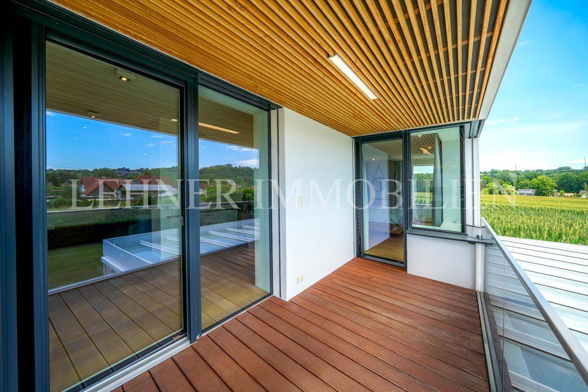 Moderner Balkon mit Holzdeck, Glasgeländer und weitem Blick ins Grüne.