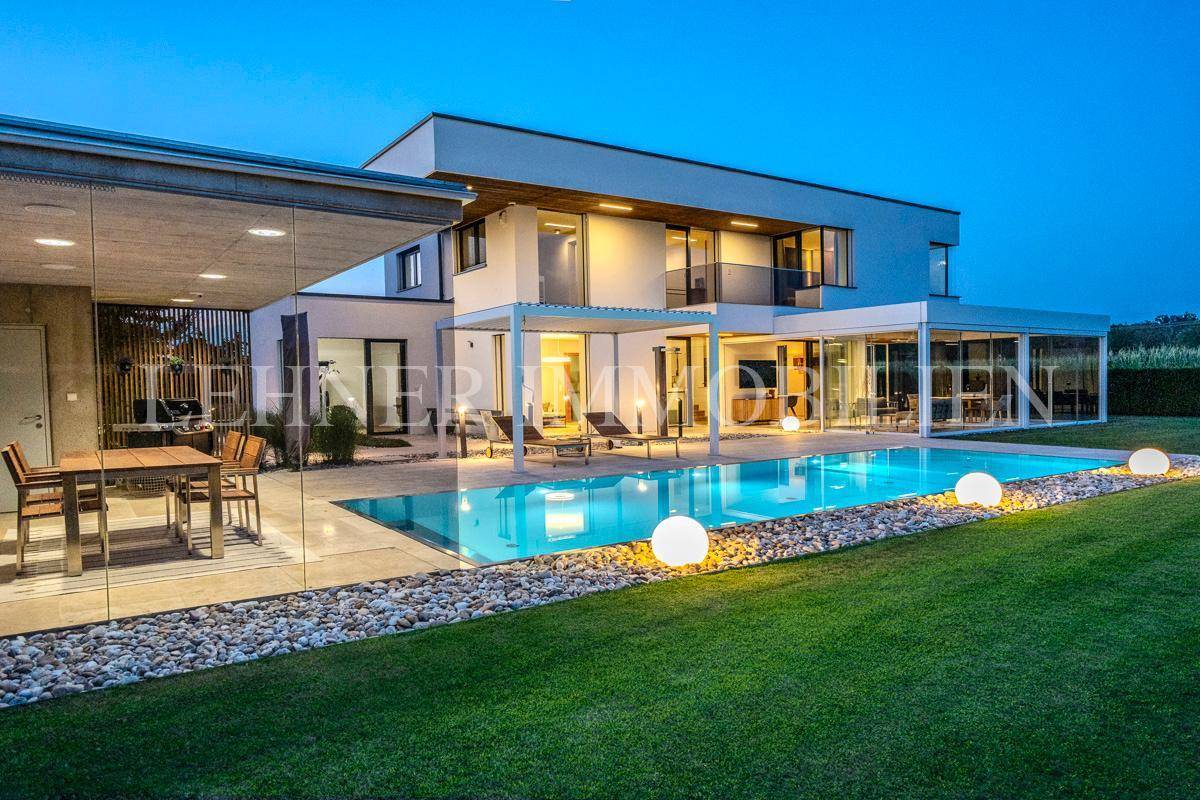 Weitläufiger Garten und Poolbereich bei Dämmerung, mit stimmungsvoller Beleuchtung und moderner Villa.
