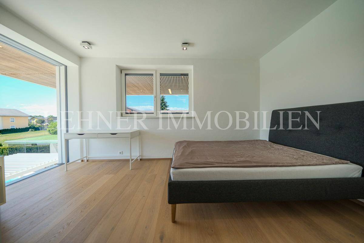 Helles Schlafzimmer mit Schreibtisch, Bett und großen Fenstern mit Blick ins Freie.