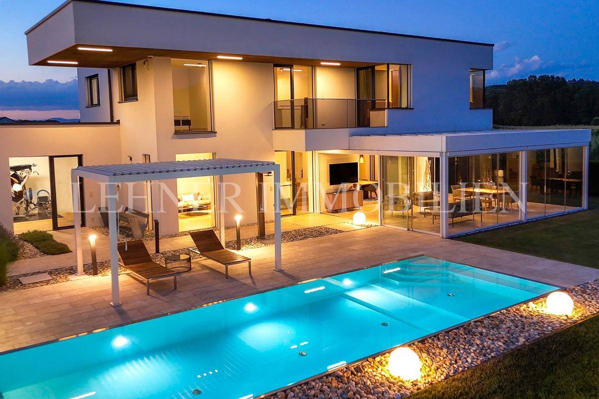 Stilvoll beleuchtete Terrasse und Poolbereich bei Nacht, mit Liegestühlen unter einer Pergola.