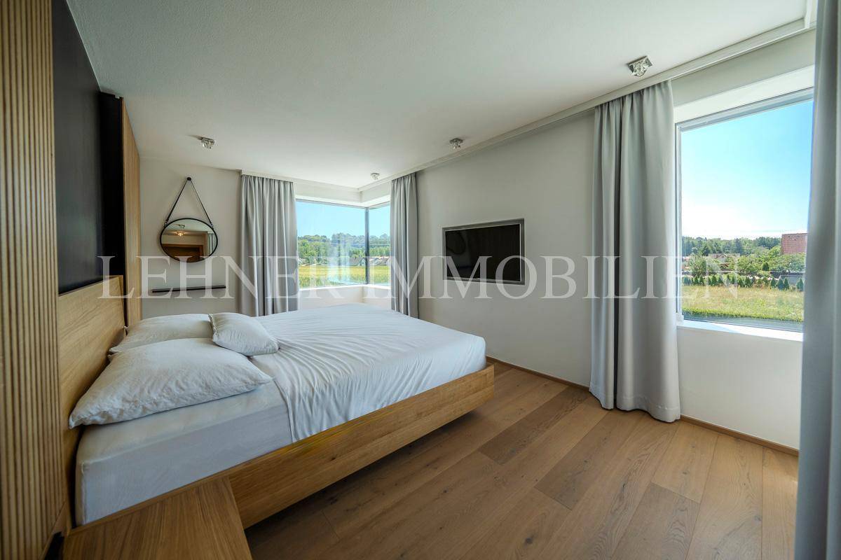 Geräumiges Schlafzimmer mit Holzboden, großen Fenstern und Blick auf die grüne Umgebung.