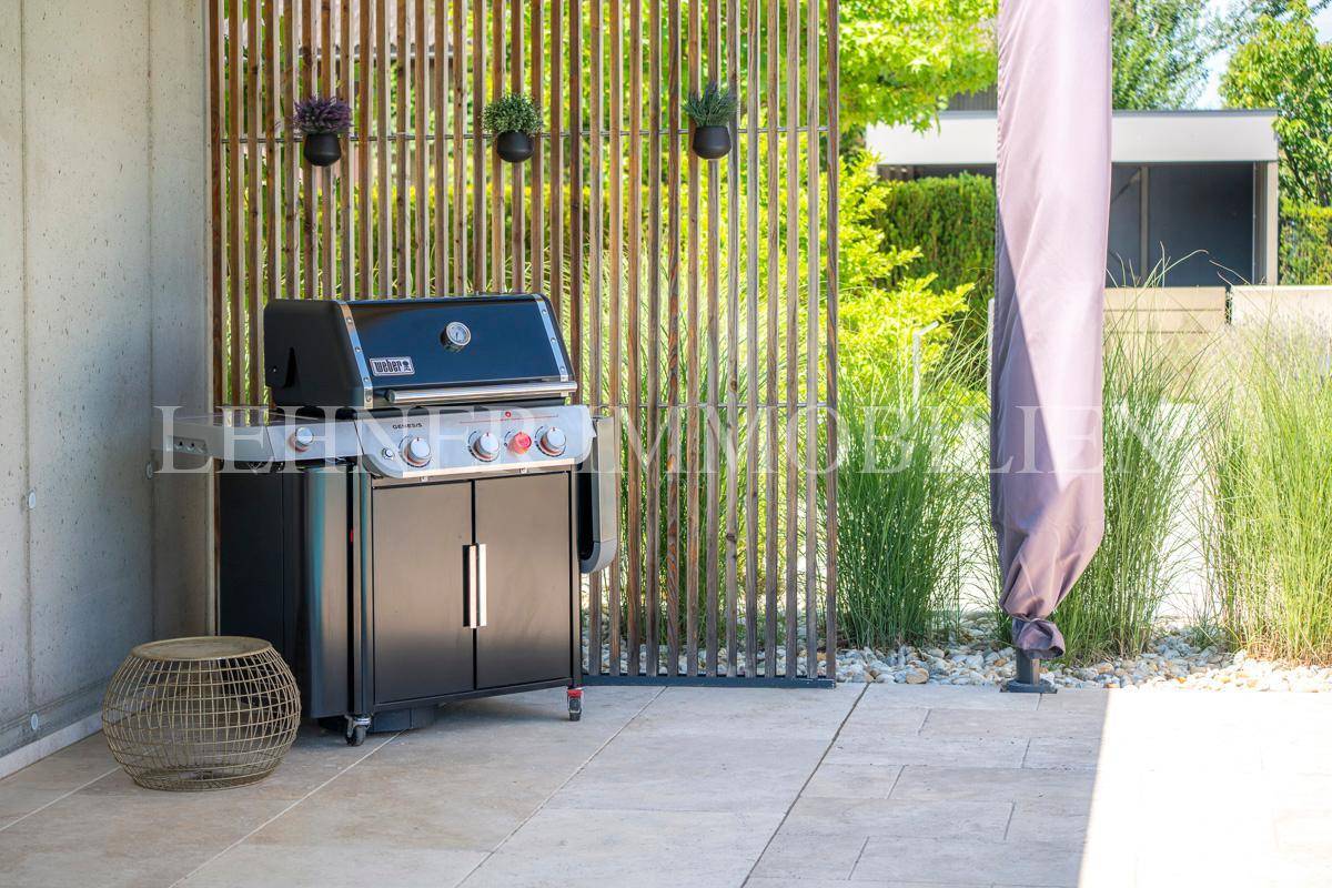 Grillbereich im Garten mit modernem Gasgrill und Holzwand.