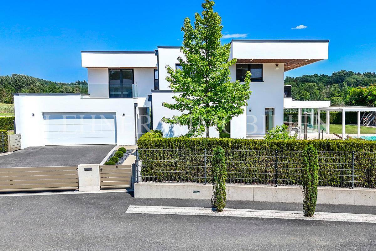 Elegante moderne Villa mit Garage, Zufahrt und grüner Bepflanzung.