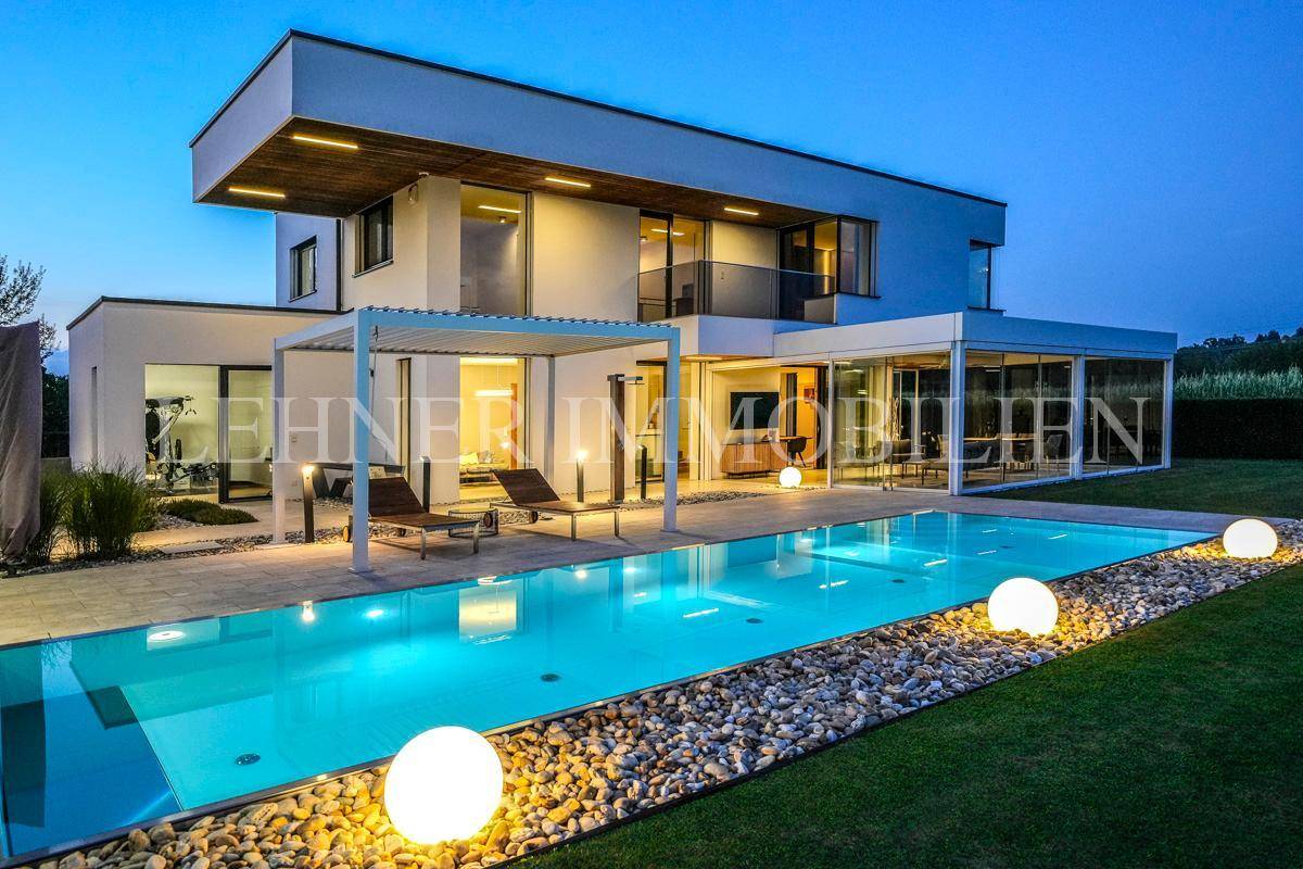 Beleuchteter Gartenbereich bei Nacht mit modernem Pool, stilvollen Kugelleuchten und der eleganten Villa.