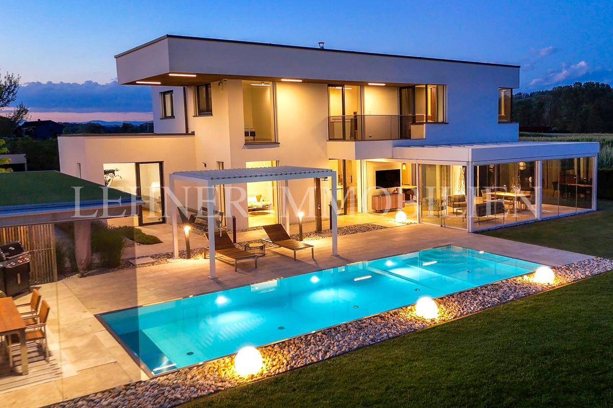 Elegante Villa mit beleuchtetem Pool und Garten bei Nacht, umgeben von einer ruhigen Landschaft.