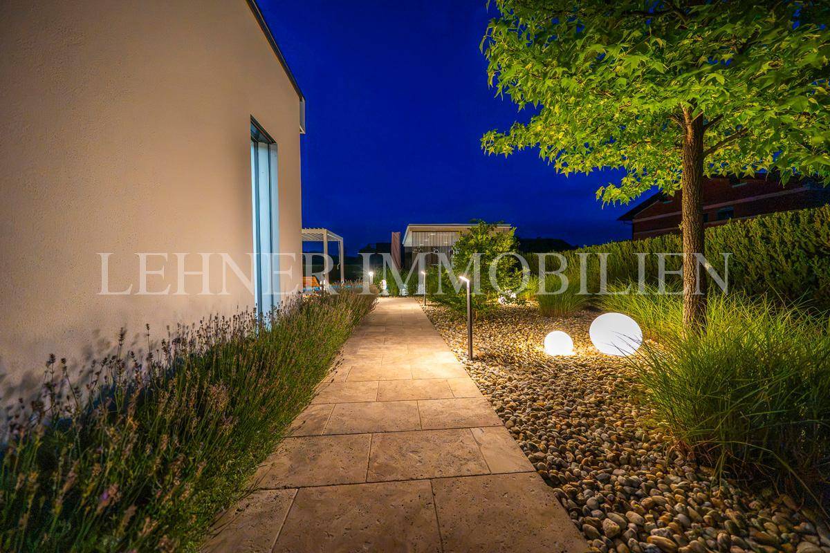 Beleuchteter Gartenweg mit Kiesbeet und dekorativen Kugelleuchten, umgeben von Pflanzen bei Nacht.