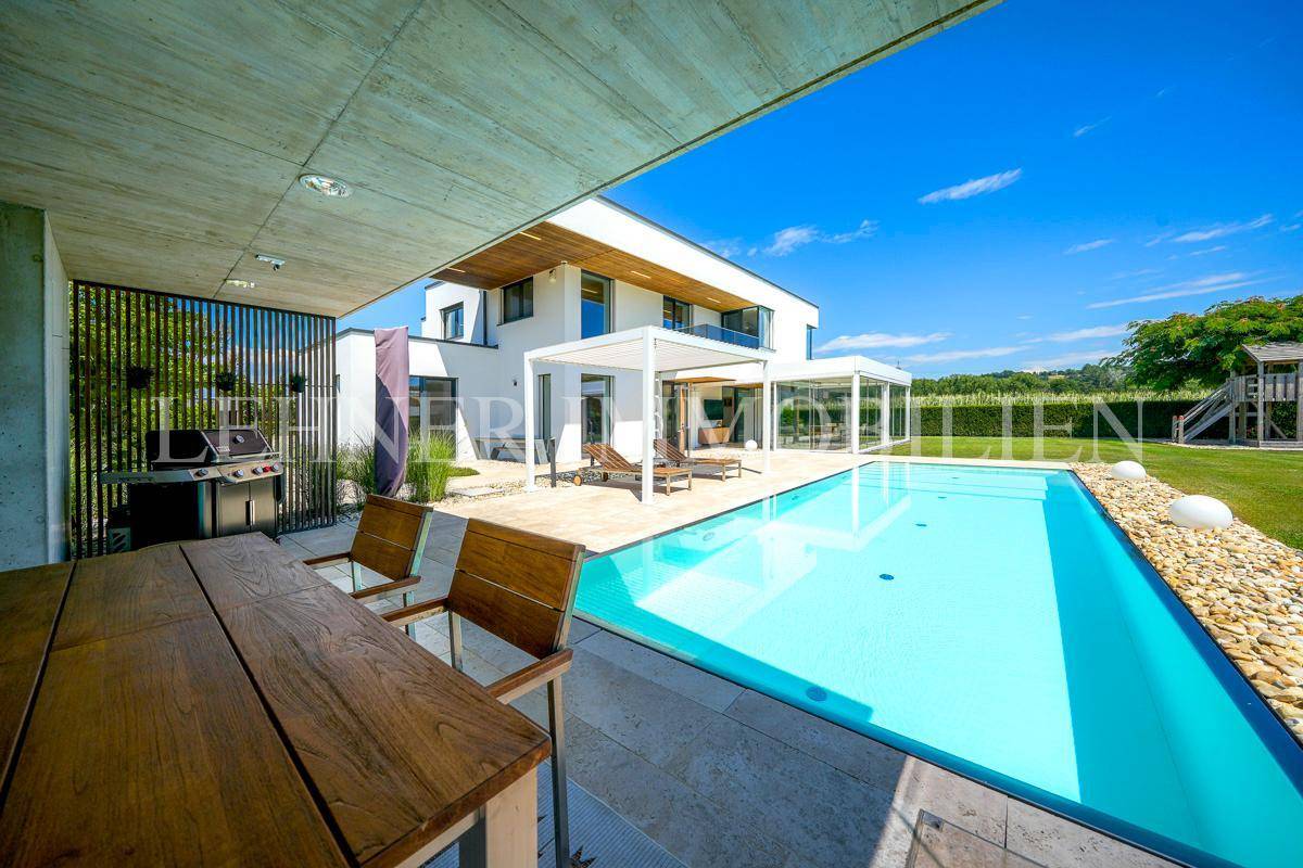 Überdachter Essbereich im Freien mit Grill und Blick auf den modernen Pool und die Villa.
