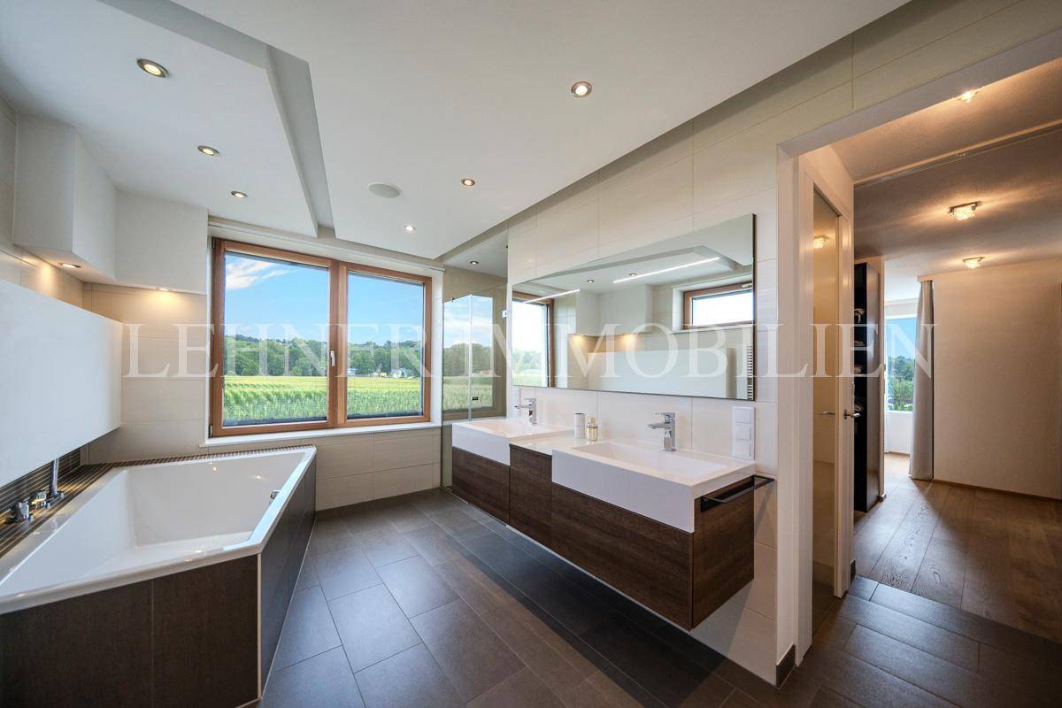 Elegantes Badezimmer mit Badewanne, Doppelwaschbecken und großem Fenster mit Blick ins Grüne.