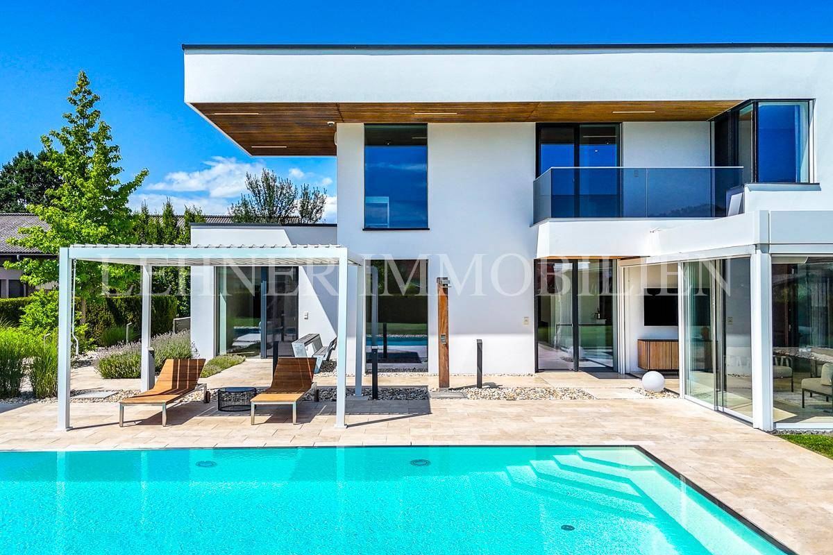 Detailansicht der modernen Villa mit Pool, Pergola und Liegestühlen auf der sonnigen Terrasse.