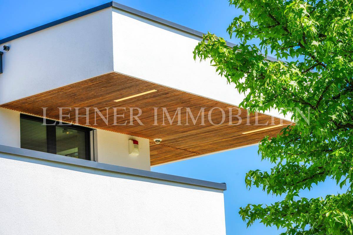 Detail der modernen Fassade mit weißem Putz und einer eleganten Holzverkleidung unter dem Dachüberstand.
