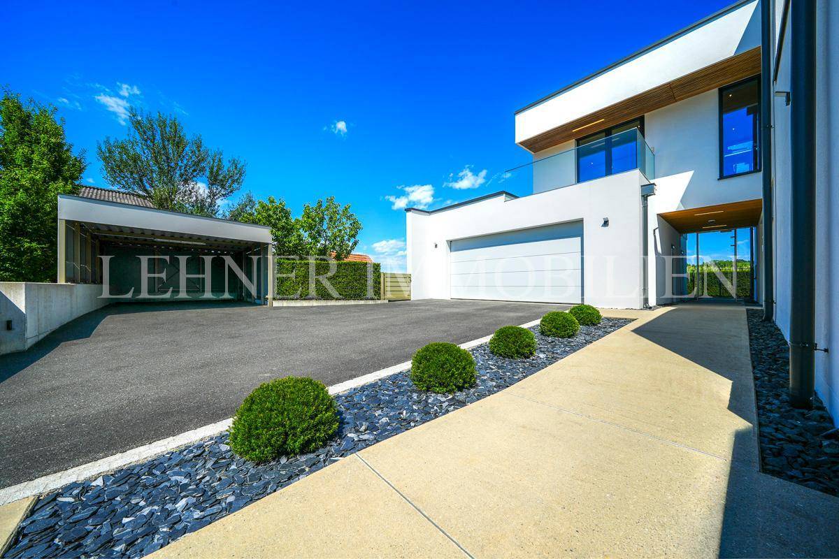 Geräumige Auffahrt mit Carport und modernem Design, umgeben von grünen Sträuchern und Kies.