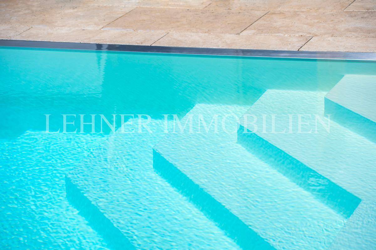 Nahaufnahme des Pools mit hellblauem Wasser und breiten Einstiegsstufen, umgeben von hellen Fliesen.