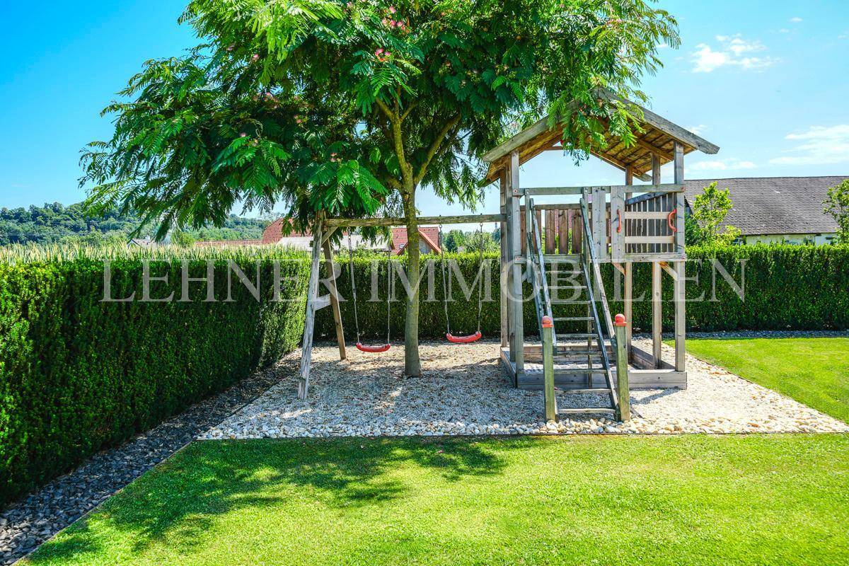 Kinderspielplatz im Garten mit Schaukeln und einem Spielhaus, umgeben von Rasen und Hecke.