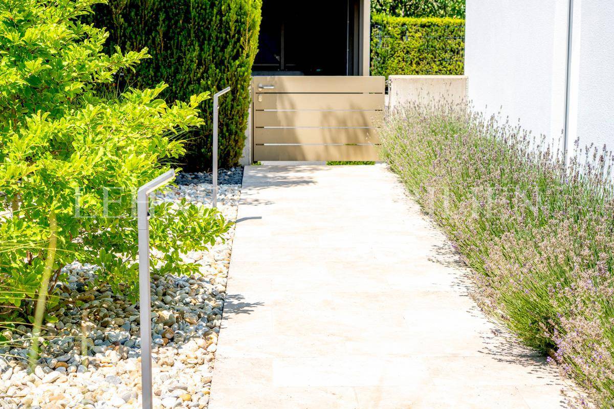 Gepflasterter Weg mit Lavendel und Kies, der zu einem Gartentor führt.