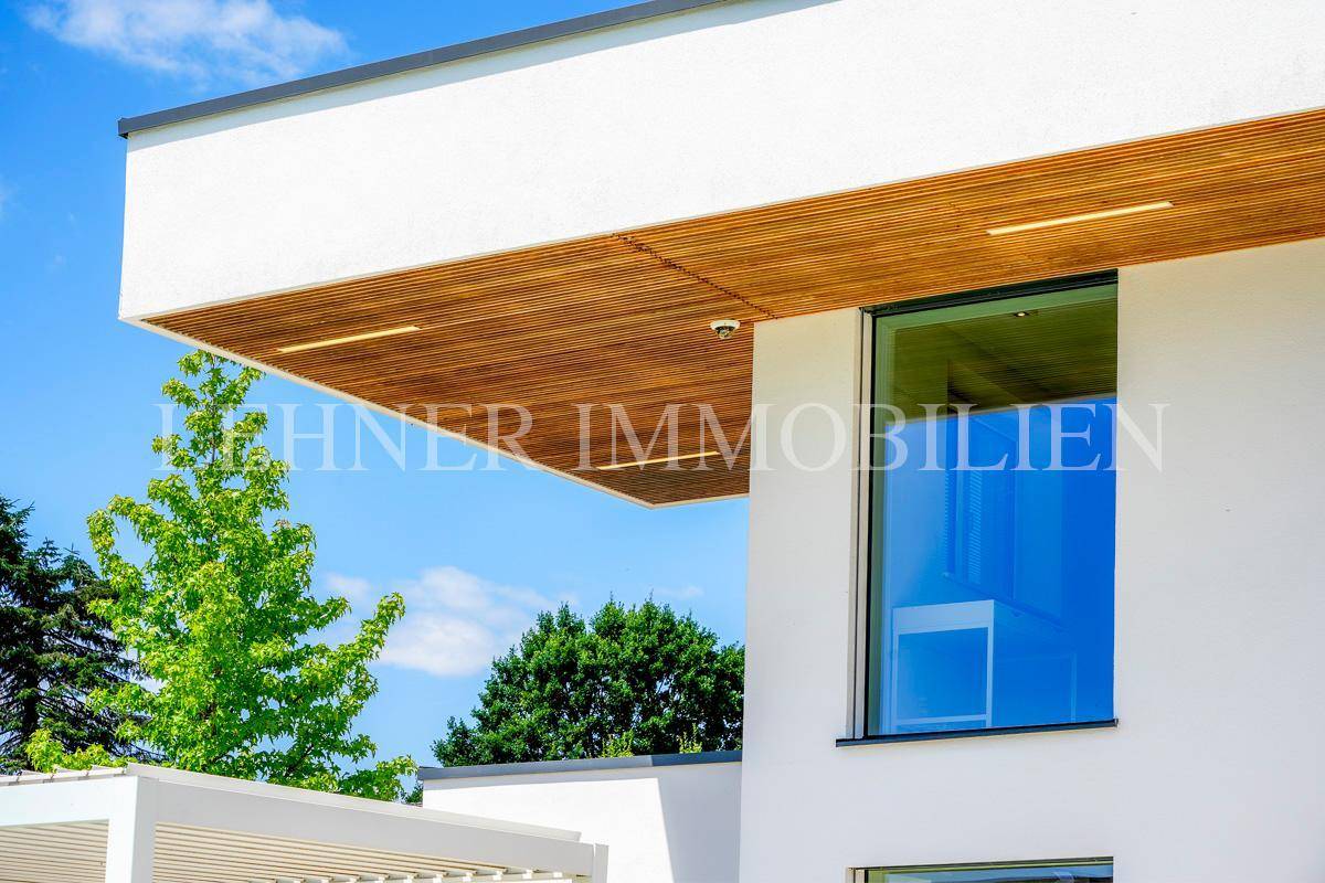 Detail der modernen Architektur mit großen Fenstern und einer stilvollen Holzverkleidung unter dem Dach.