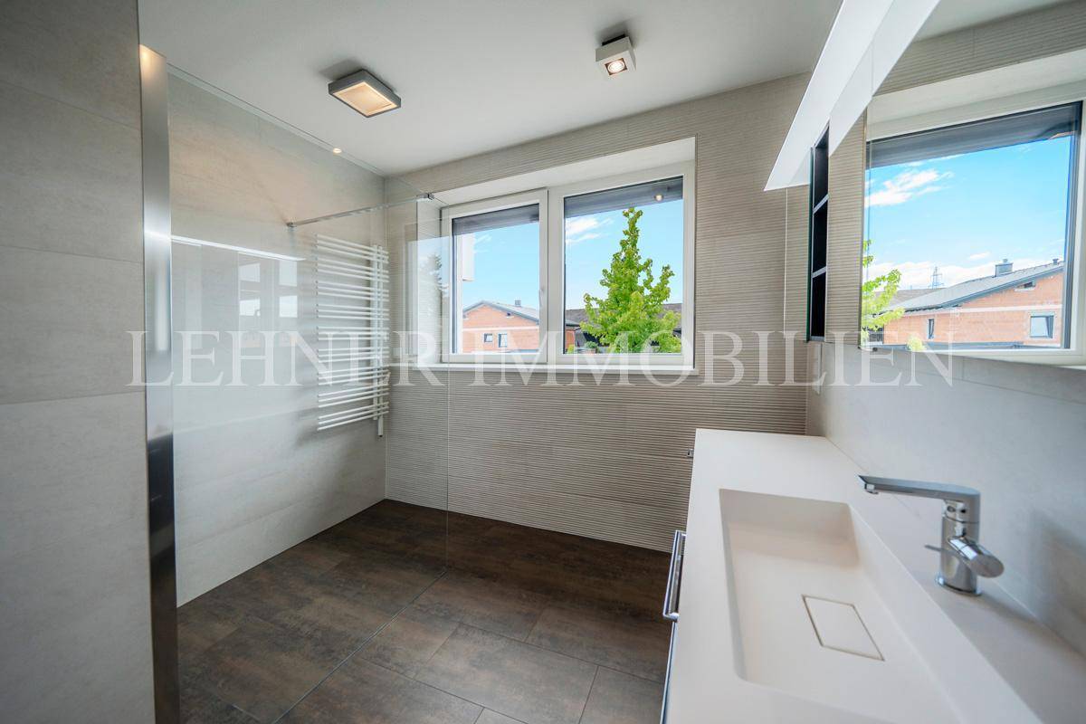 Helles Badezimmer mit begehbarer Dusche, Waschbecken und Fenster mit Blick nach draußen.