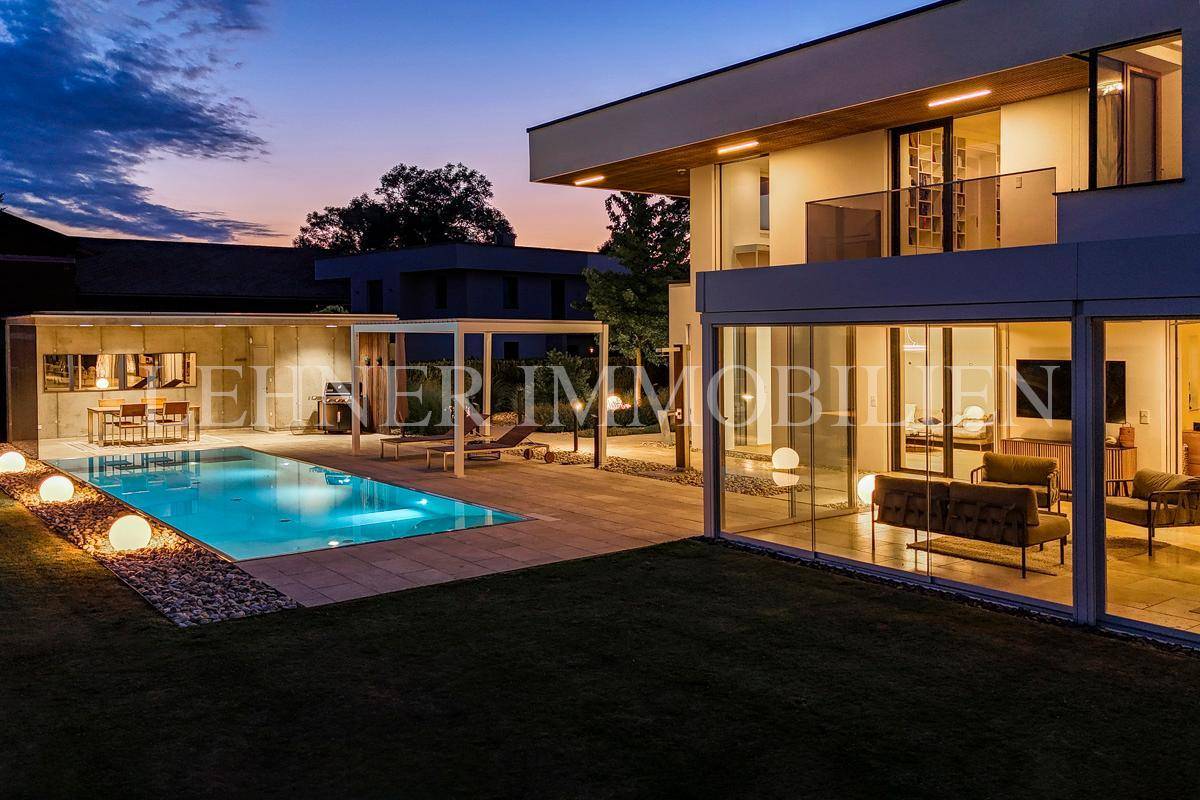 Moderne Villa mit beleuchtetem Pool und verglastem Wohnbereich, der sich zum Garten öffnet.