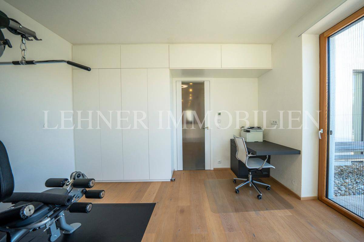 Heller Raum mit Fitnessgeräten, integrierten Schränken und Zugang zum Außenbereich.