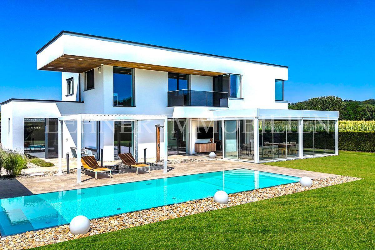Panoramablick auf die moderne Villa mit großem Pool und gepflegtem Garten unter blauem Himmel.