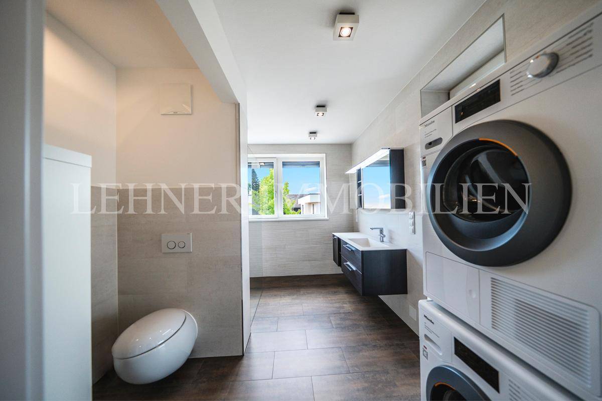Modernes Badezimmer mit Waschmaschine, Trockner, Waschbecken und Fenster.