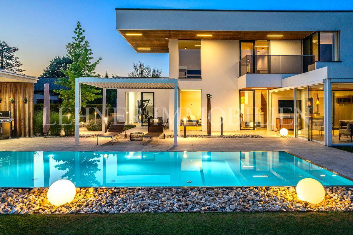 Nahaufnahme des beleuchteten Pools und der modernen Villa bei Einbruch der Dunkelheit.