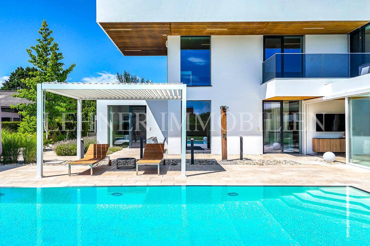 Detailansicht des Pools mit Außendusche und Sonnenliegen unter einer Pergola, umgeben von mediterranen Pflanzen.