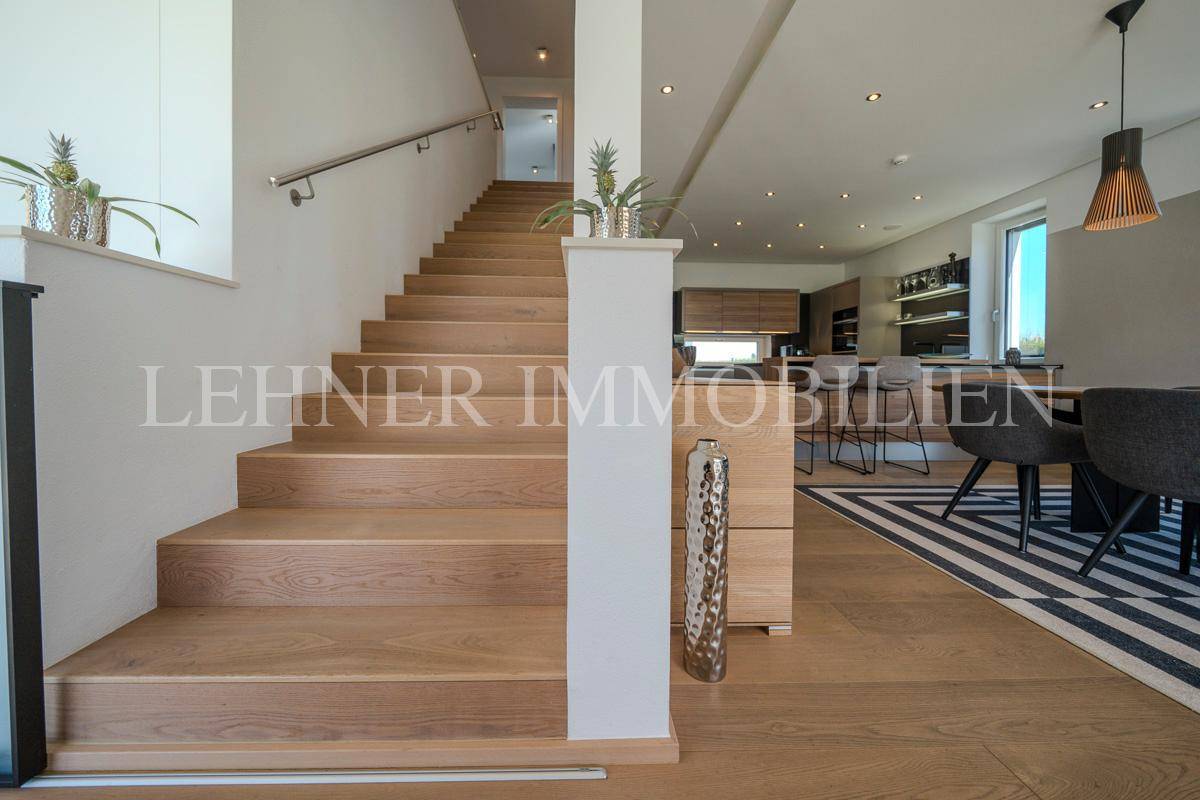 Elegante Holztreppe führt in die obere Etage, mit Blick auf den offenen Wohn- und Essbereich.