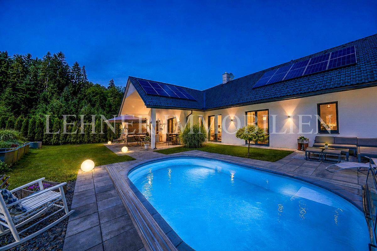 Modernes Haus bei Nacht mit beleuchtetem Pool, Terrasse und Solaranlage auf dem Dach.