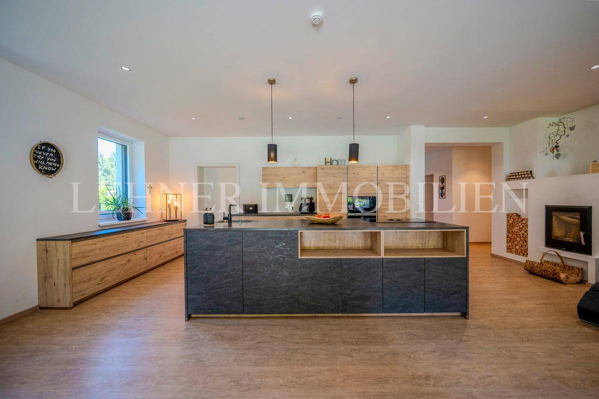 Geräumige Küche mit dunkler Kücheninsel, Holzfronten und einem modernen Kamin im Hintergrund.