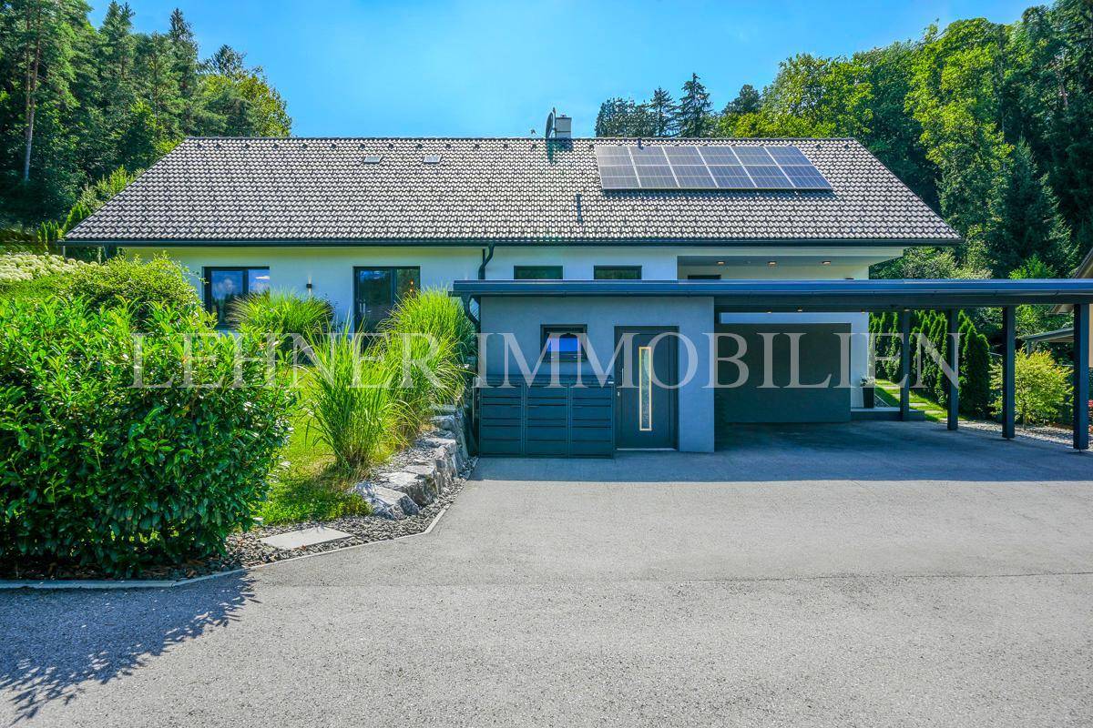 Moderne Hausfassade mit Carport und Photovoltaikanlage auf dem Dach in grüner Umgebung.