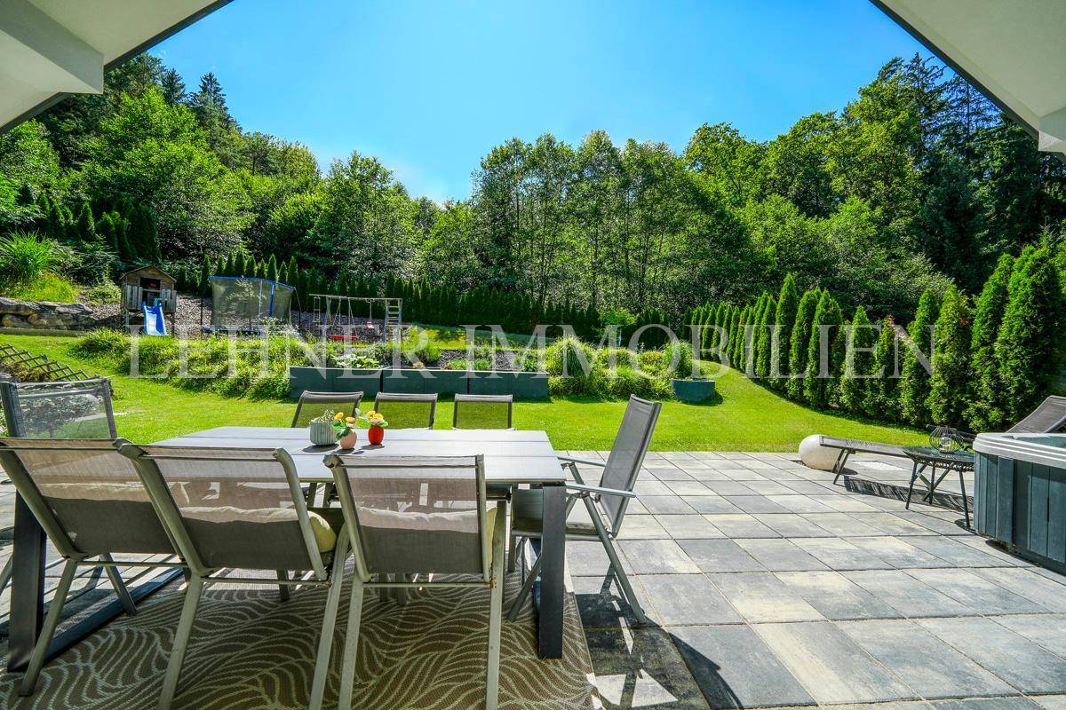 Geräumige Terrasse mit Esstisch und Stühlen, umgeben von einem grünen Garten und Bäumen.