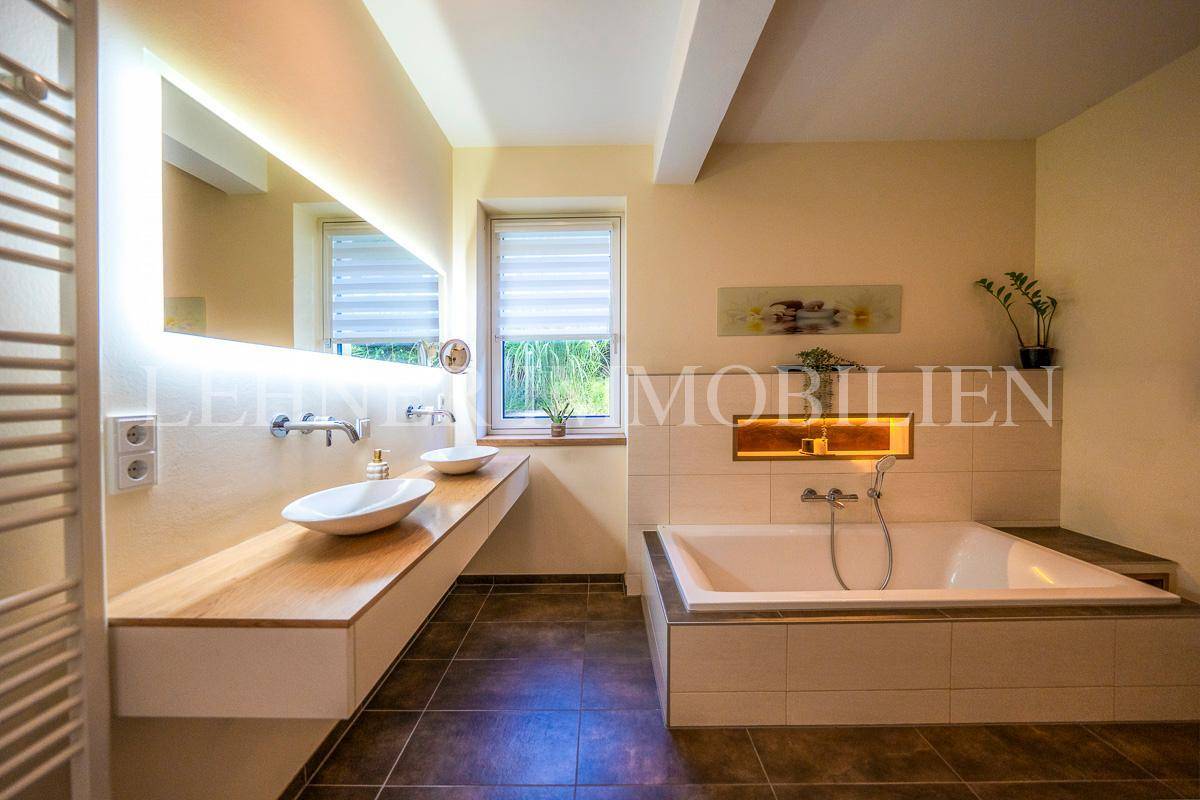 Modernes Badezimmer mit großer Badewanne, Doppelwaschbecken und beleuchtetem Spiegel.