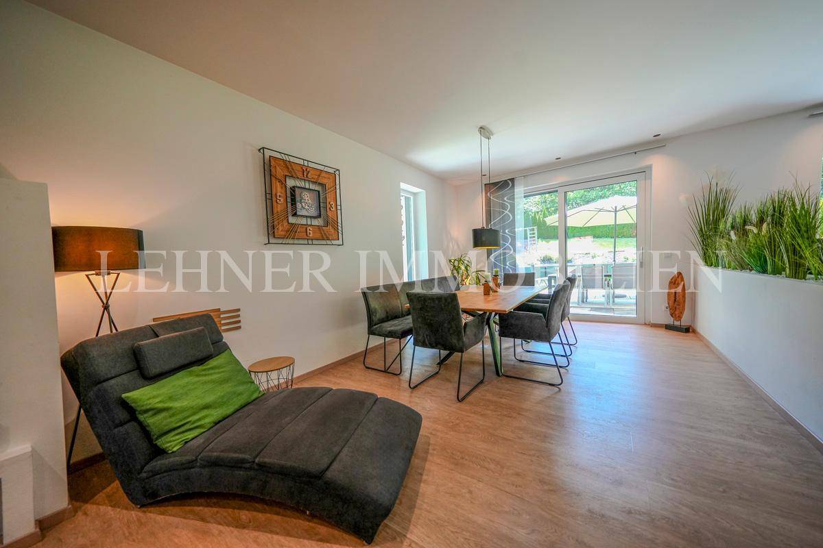 Helles Wohn- und Esszimmer mit Holzboden, bequemer Liege und Zugang zur Terrasse.