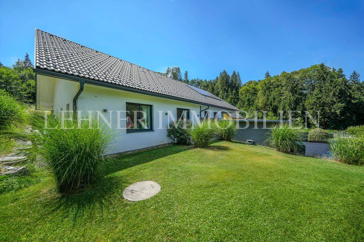 Modernes Einfamilienhaus mit gepflegtem Garten und grüner Umgebung unter blauem Himmel.