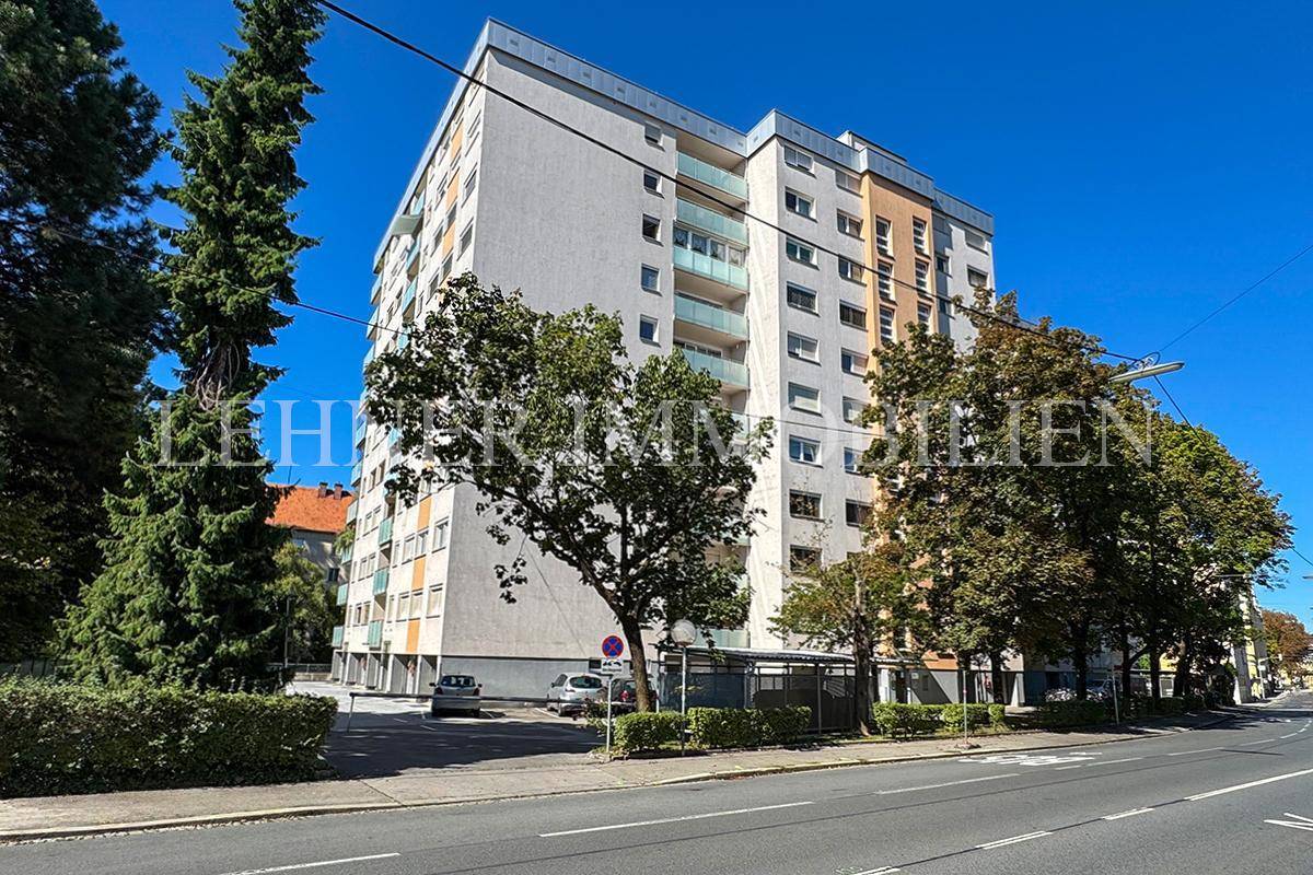 Modernes Mehrfamilienhaus mit Balkonen und Bäumen an einer ruhigen Straße gelegen.