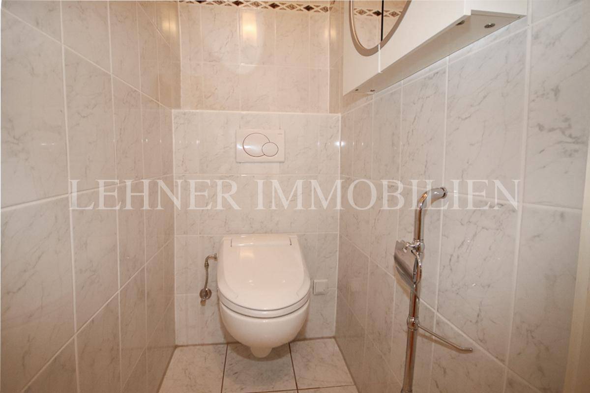 Separates WC mit wandhängender Toilette und hellen Fliesen an Wänden und Boden.