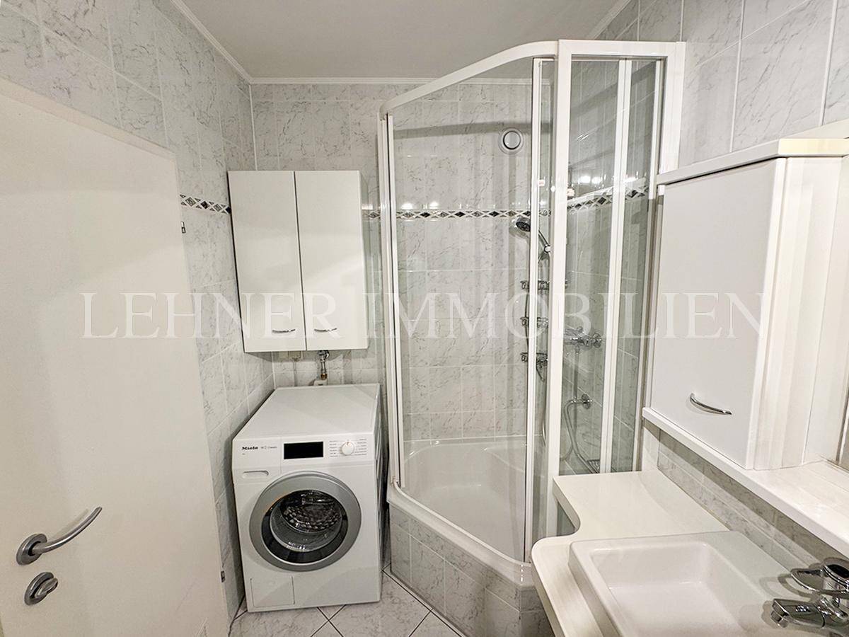 Badezimmer mit Duschkabine, Waschmaschine und praktischen Ablagemöglichkeiten.