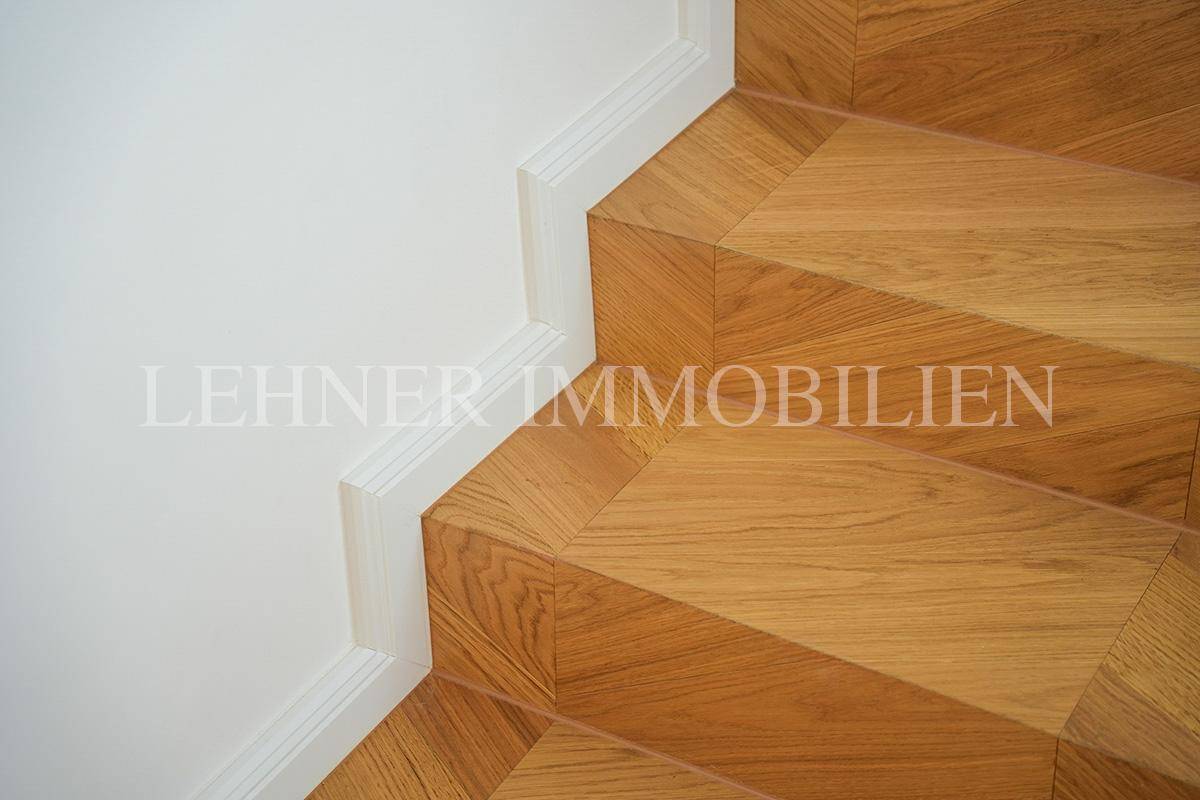 Detailaufnahme der Holztreppe mit Fischgrätmuster und weißer Sockelleiste.