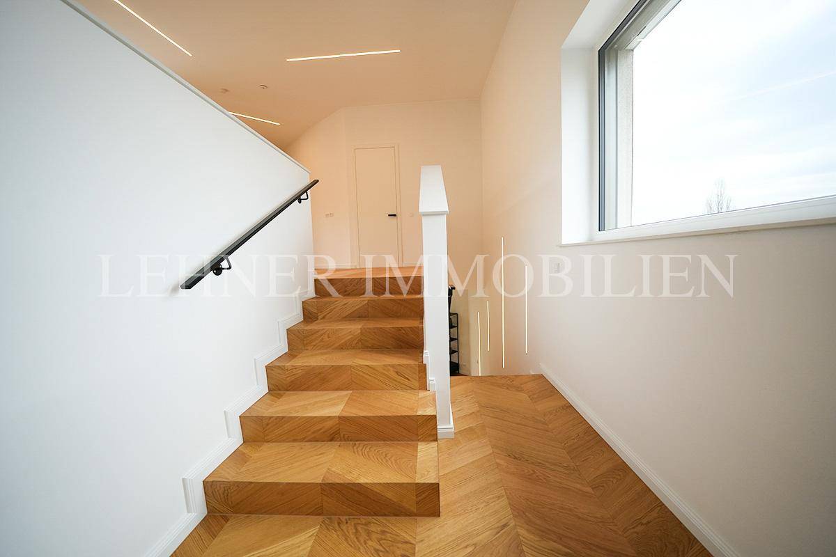 Heller Treppenaufgang mit Holzstufen, großem Fenster und Blick in den oberen Bereich.