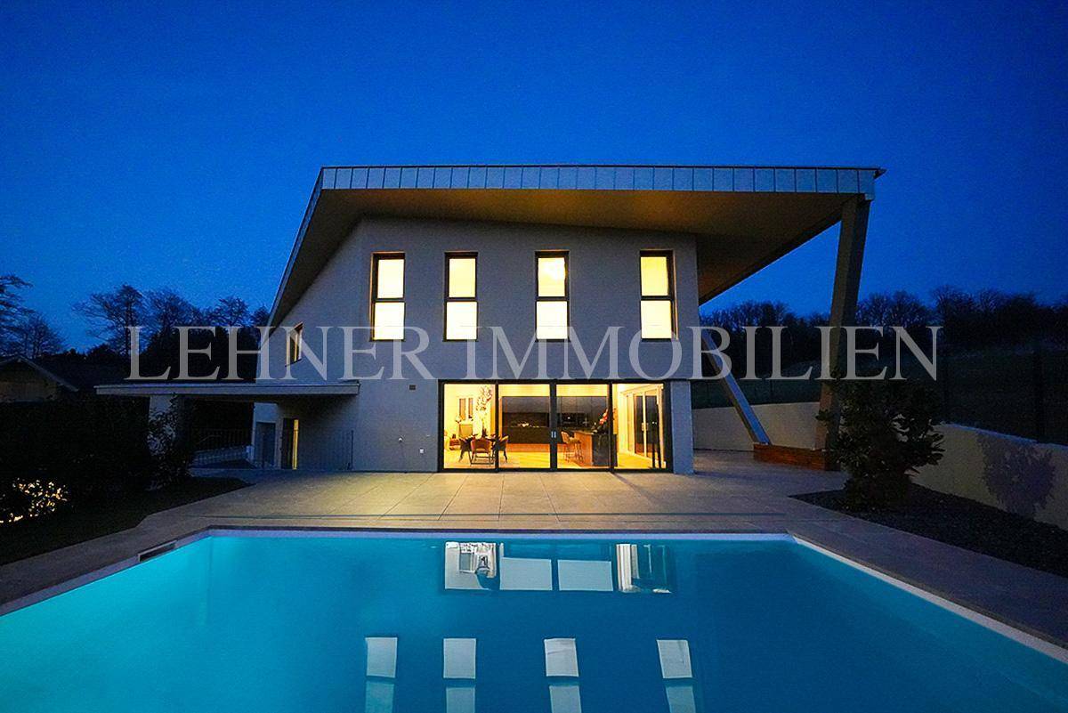 Beleuchtetes modernes Haus und Pool bei Dämmerung, mit warmem Licht aus den Innenräumen.