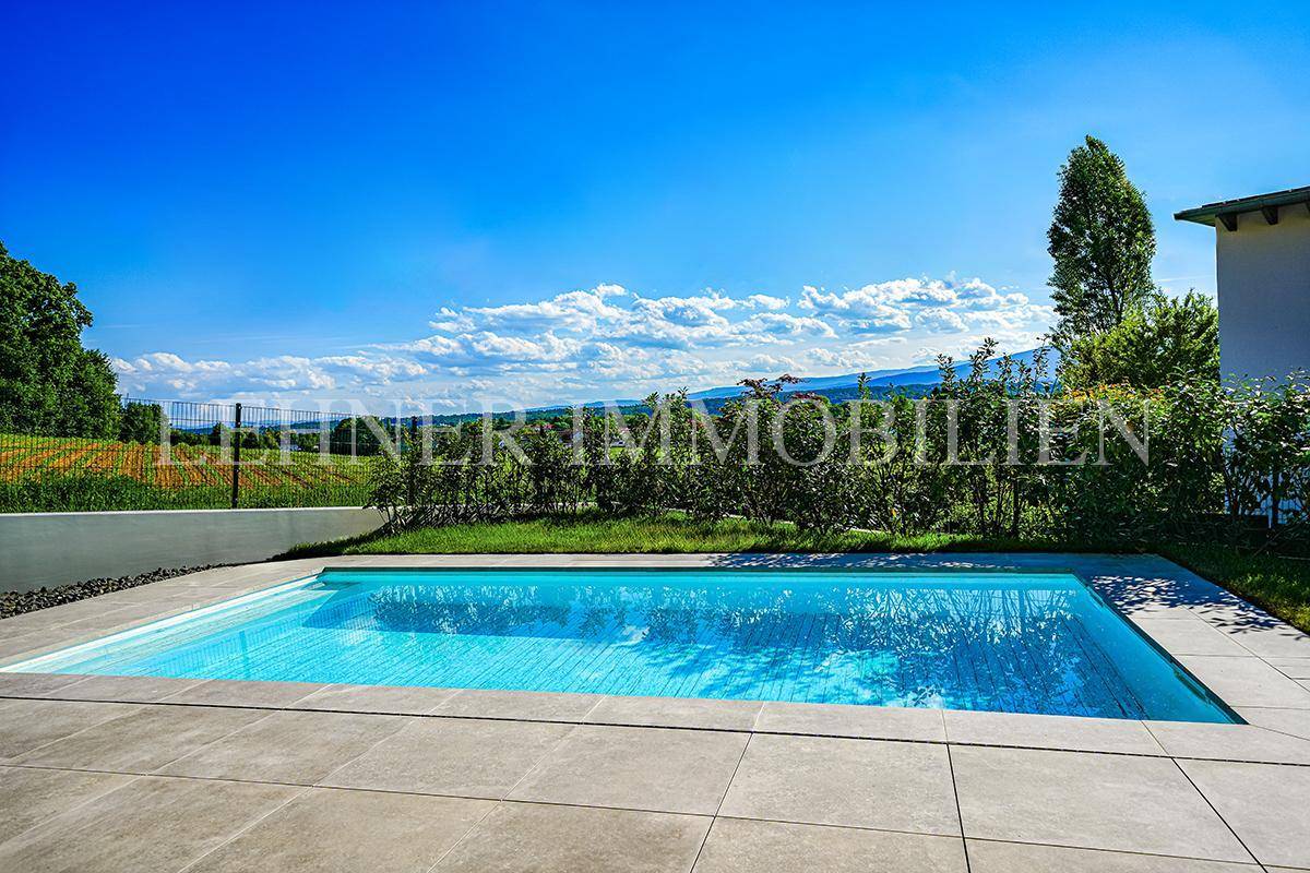 Blauer Swimmingpool mit gefliestem Rand und weitem Blick über die grüne Landschaft bis zum Horizont.