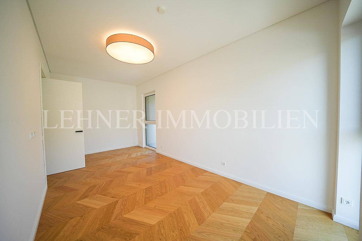 Modernes, helles Zimmer mit Fischgrätparkett und Zugang zu einem Außenbereich durch eine Fenstertür.
