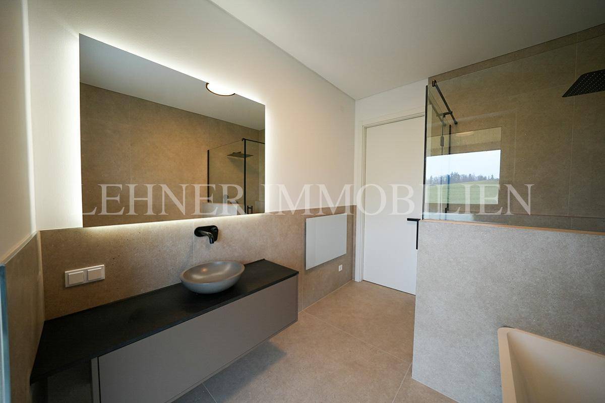 Geräumiges Badezimmer mit großer Dusche, Badewanne und beleuchtetem Spiegel, modern gefliest.