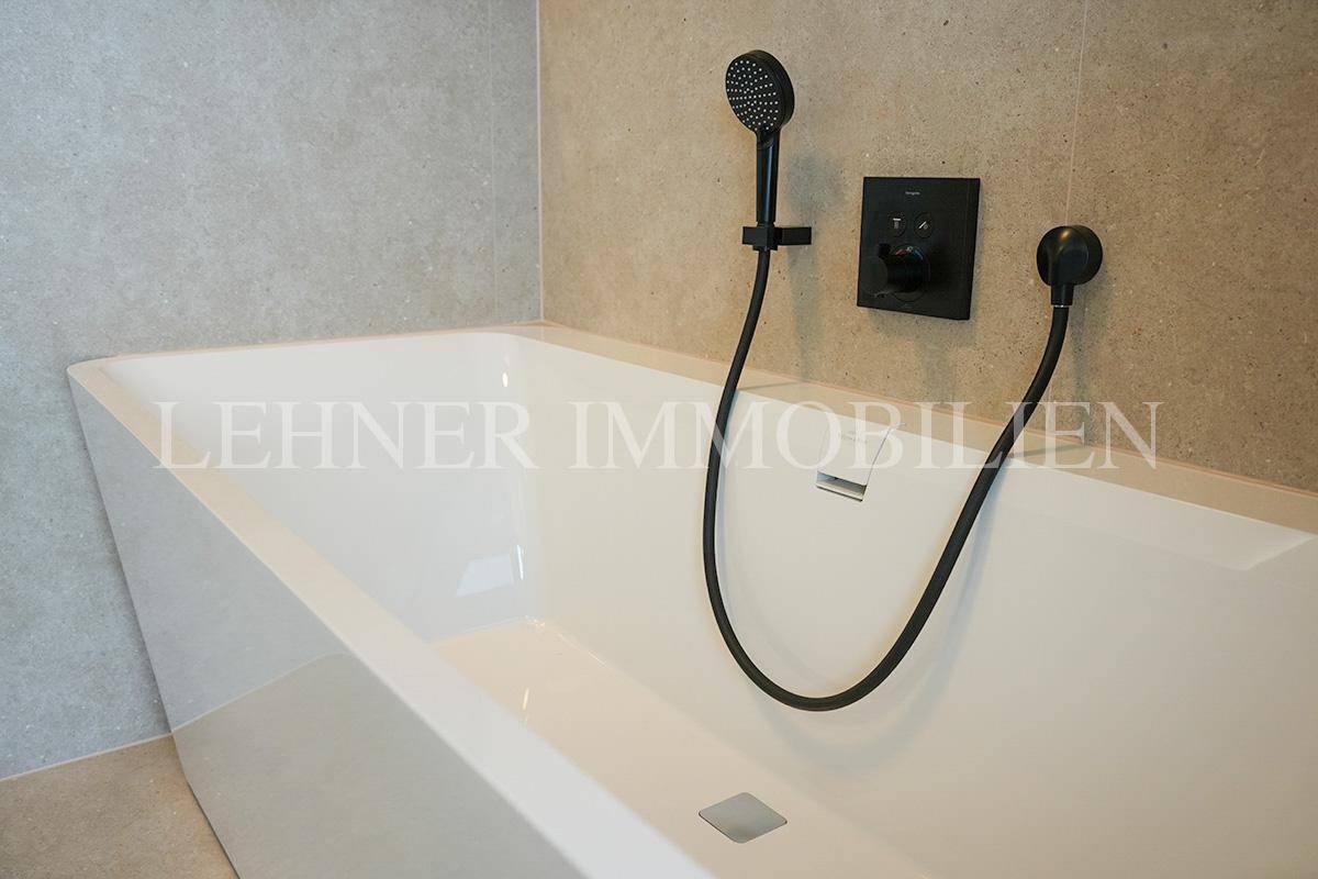 Detailaufnahme der modernen Badewannenarmatur mit Handbrause in Schwarz, integriert in die Wanne.