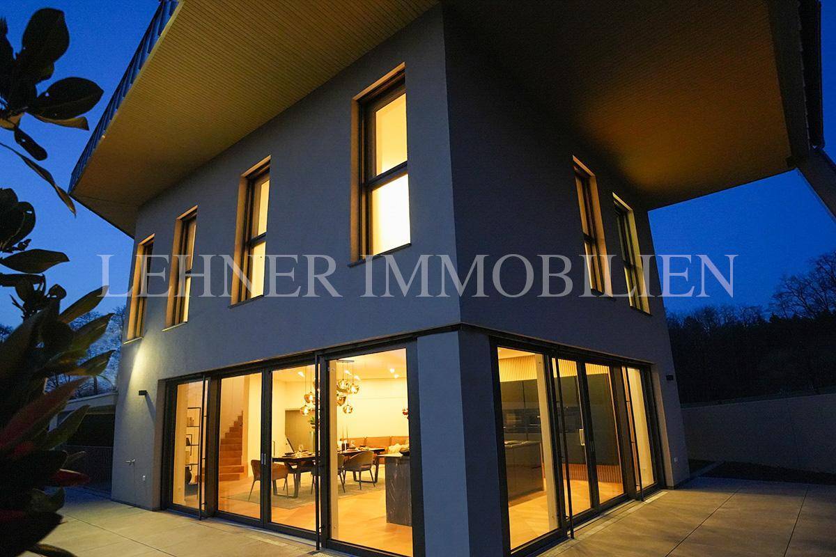 Moderne Architektur des Hauses bei Nacht, mit beleuchteten Innenräumen und großen Glasfronten.