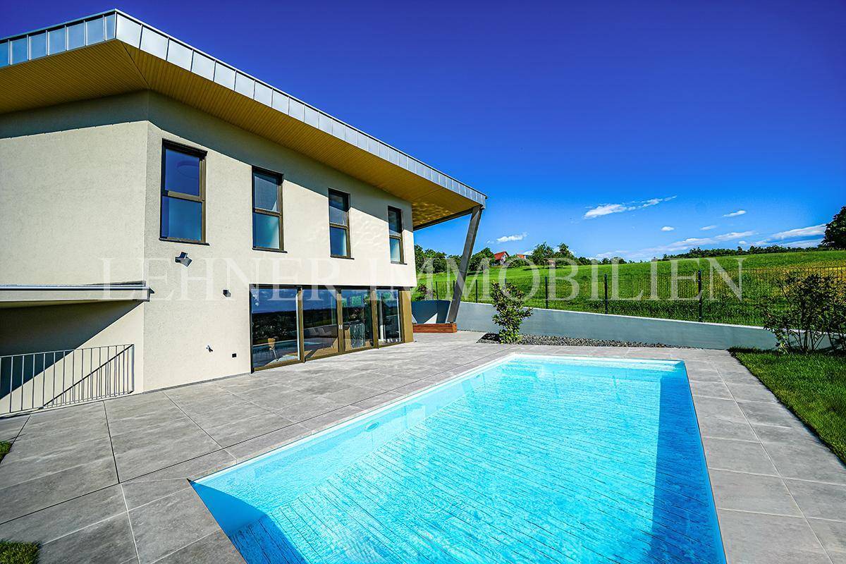 Modernes Haus mit markanter Architektur, großem Pool und weitläufiger Terrasse, umgeben von Natur.
